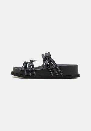 Zwarte slidesandalen met een brede band, voorzien van decoratieve knoopaccenten en contrasterende witte stiksels. Gemaakt van flexibel synthetisch materiaal.