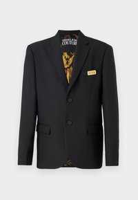 Črn blazer z dvema gumboma, zareznimi klapnicami, sprednjimi žepi in dekorativno zlatim logotipom. Notranjost je obložena s patterned zlato podlogo.