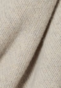 Cremefarbener Wollstoff mit einem strukturierten, gestrickten Muster. Die Oberfläche ist weich und leicht fusselig, zeigt natürliche Fasern und subtile Variationen.