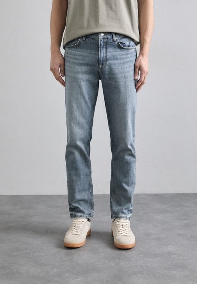 Lysblå denim jeans med lige pasform, diskret falmning, fem lommer og knaplukning, parret med beige sneakers.
