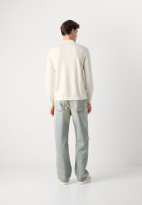 Maglione chiaro in crema con scollo tondo, polsini a costine e dettaglio di cucitura. Abbinato a jeans in denim blu sbiadito e calzature chiare.