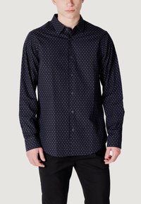 Camicia button-up blu scuro con pois bianchi, maniche lunghe, colletto a punta e orlo arrotondato. Realizzata in tessuto liscio con una leggera lucentezza.