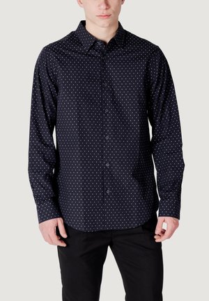 Camicia button-up blu scuro con pois bianchi, maniche lunghe, colletto a punta e orlo arrotondato. Realizzata in tessuto liscio con una leggera lucentezza.
