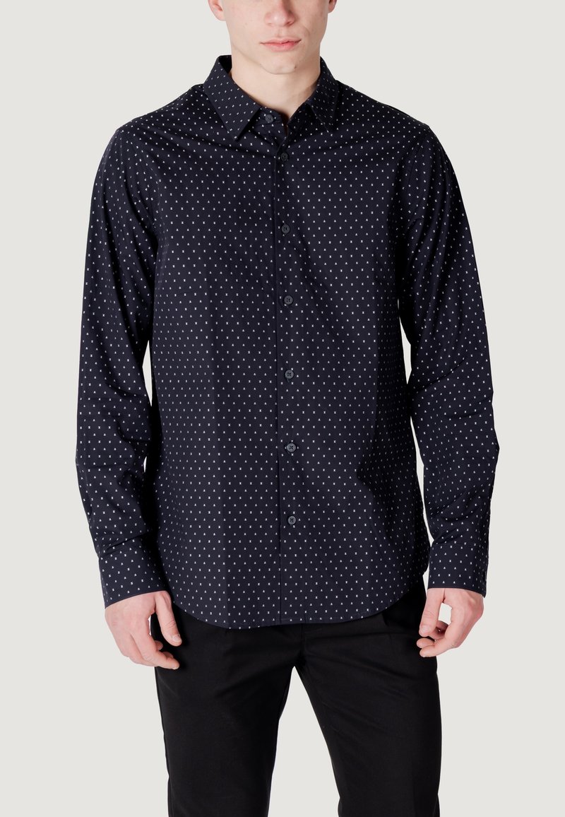 Camicia button-up blu scuro con pois bianchi, maniche lunghe, colletto a punta e orlo arrotondato. Realizzata in tessuto liscio con una leggera lucentezza.