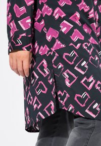 Schwarzes Hemd mit Knöpfen, das ein pink-weißes, abstraktes Herzmuster zeigt. Es hat einen leicht geschwungenen Saum und lange Ärmel.
