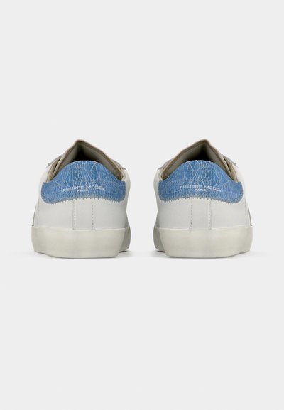 Λευκά αθλητικά παπούτσια με μπλε σκασμένη δερμάτινη λεπτομέρεια, γκρι γλώσσα και μπεζ σόλες. Διαθέτουν ραμμένες λεπτομέρειες και μινιμαλιστικό σχεδιασμό.