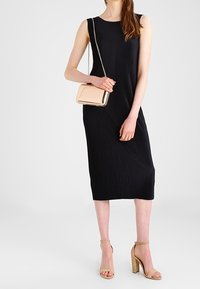 Černé vroubkované midi šaty s elegantním střihem, doplněné béžovými sandály na blokovém podpatku a malou metallic-crossbody kabelkou.