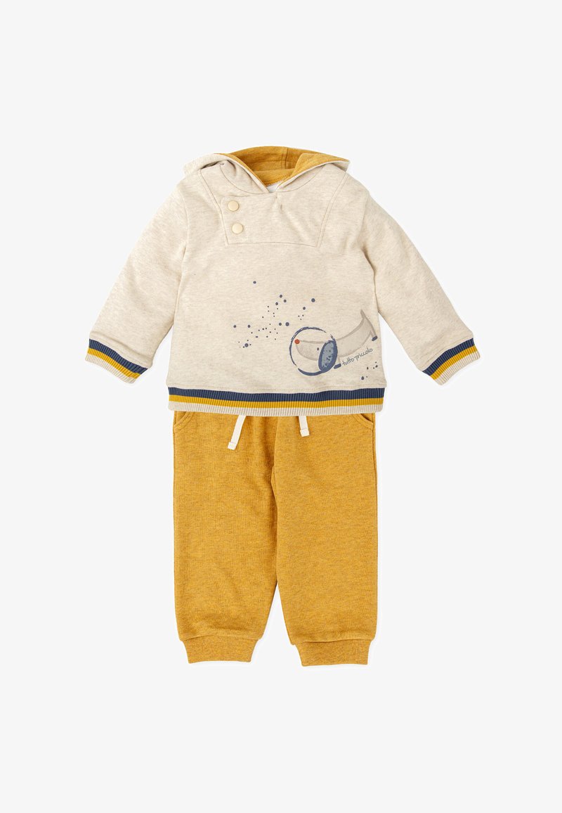 Sudadera con capucha en beige claro con acentos en azul oscuro y amarillo, que presenta un gráfico de un telescopio. Combinada con pantalones de chándal de color mostaza.