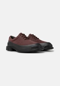 Scarpe in suede bordeaux con suole in gomma nera, dotate di lacci e di un design rigato, posizionate su uno sfondo chiaro.