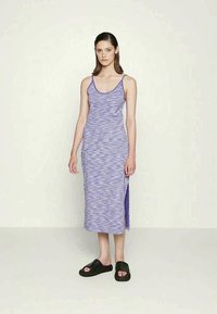 Vestuário roxo sem mangas com um padrão ondulado, comprimento abaixo do joelho, racha lateral e um design justo. Usado com sandálias pretas.