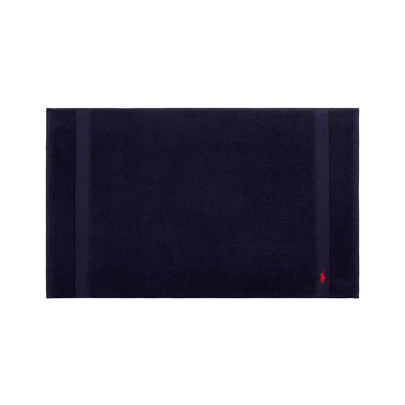 Tapis de bain en coton bleu marine à surface texturée, présentant deux rayures verticales et un petit logo rouge dans un coin.