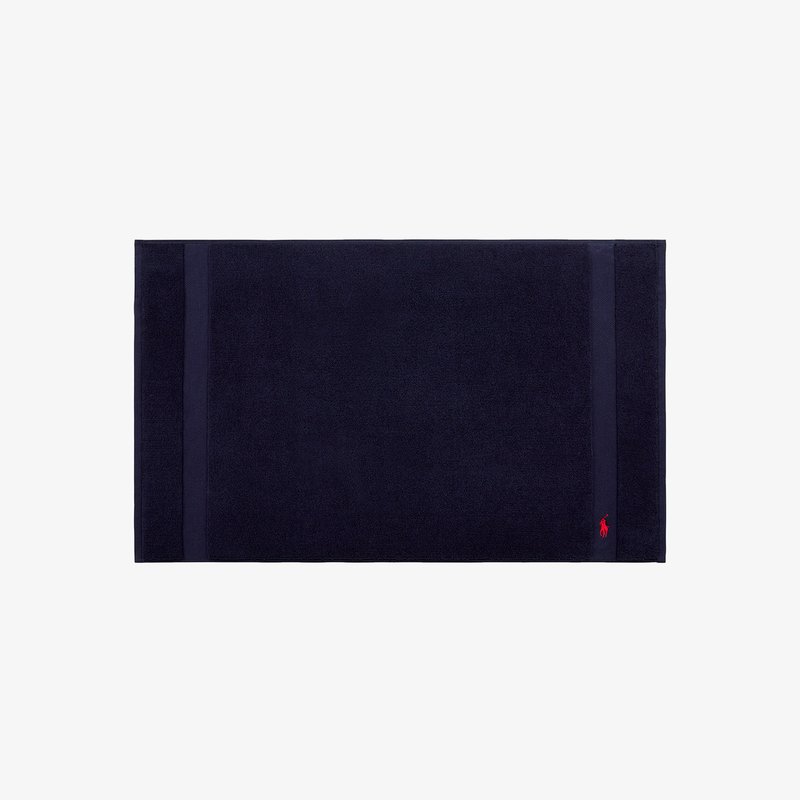 Tapis de bain en coton bleu marine à surface texturée, présentant deux rayures verticales et un petit logo rouge dans un coin.