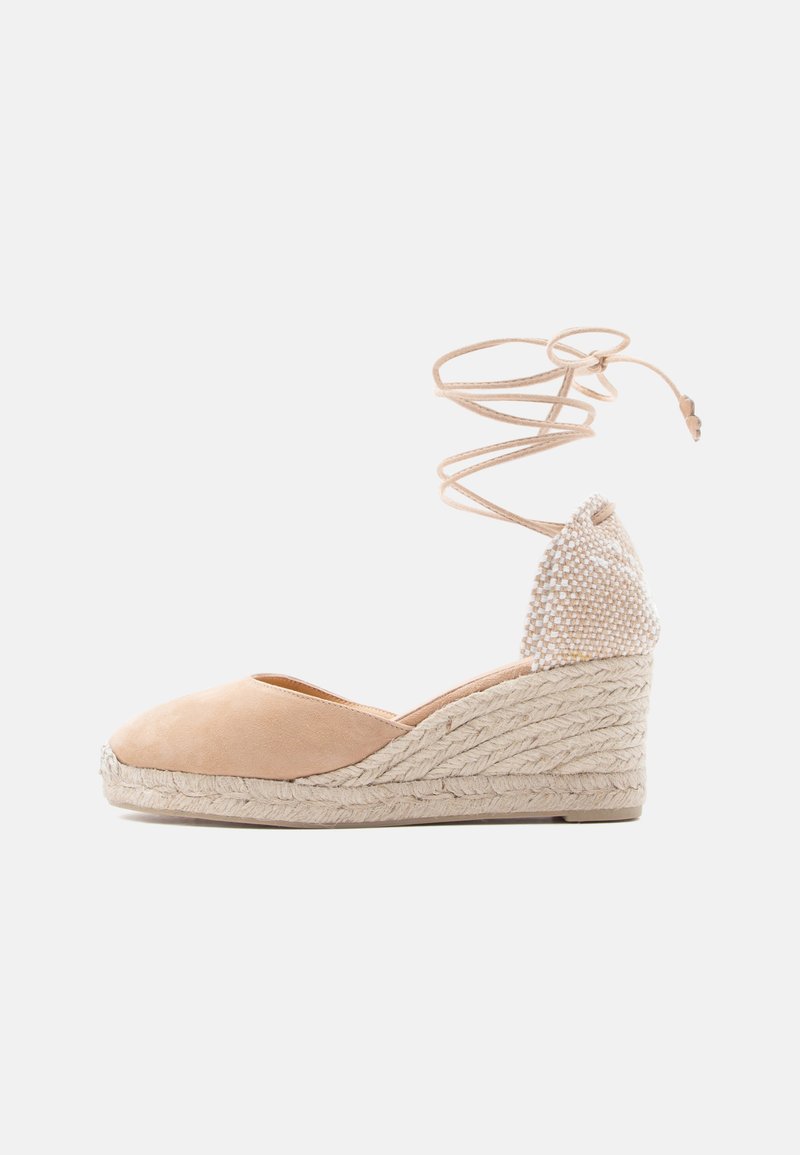 Espadrille compensée beige avec bout fermé, semelle en jute tissée, et bride à nouer autour de la cheville sur fond blanc.