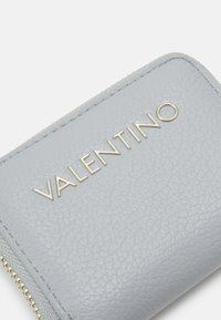 Cartera de cuero gris con acabado texturizado, que presenta el logotipo dorado "VALENTINO" y cierre de cremallera. Diseño rectangular compacto.
