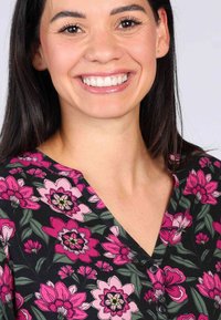 Schwarzer Stoff mit großen rosa und lila Blumenmustern sowie grünen Blättern. V-Ausschnitt-Design mit Knöpfen am Hals.