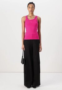 Rosa gerippte Tanktop mit rundem Ausschnitt und Logodetail, kombiniert mit schwarzen, weit geschnittenen Hosen mit Cargo-Taschen und glatter Oberfläche.