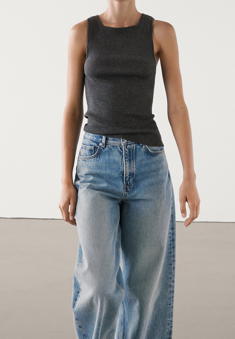 Top in cotone grigio scuro a coste con scollatura quadrata, abbinato a jeans larghi azzurri. Tessuto liscio, vestibilità aderente nella parte superiore.