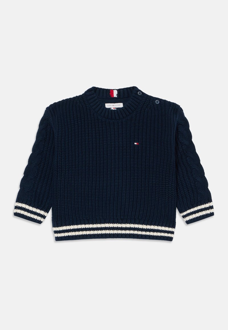 Pull en maille bleu marine avec des rayures blanches aux poignets et à l'ourlet, petit logo rouge, blanc et bleu sur la poitrine, et boutons sur l'épaule.