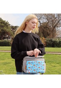 Junge Frau in schwarzem Pullover im Freien, die einen grauen Beutel mit einem blauen Hundemuster auf der Fronttasche aufzieht.