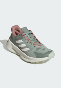 Scarpe sportive verde chiaro con tomaia in rete, dettagli rosa e strisce bianche. Presentano un colletto imbottito, suola texturizzata e lacci arancioni brillanti.