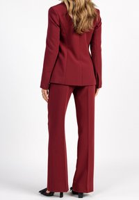 Costume sur mesure bordeaux avec un blazer ajusté et un pantalon droit. Texture lisse, fermeture à un bouton et détails de couture subtils.