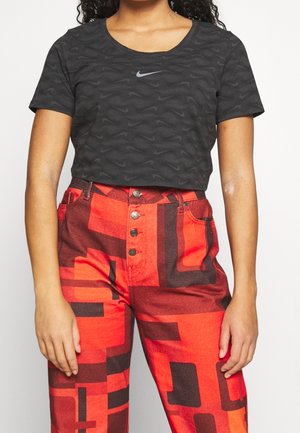Mujer vestida con una camiseta corta negra de Nike con un diseño, y pantalones rojos de cintura alta con un estampado geométrico audaz y botones delanteros.