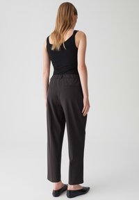 Un débardeur noir associé à un pantalon taille haute, ajusté, longueur cheville, de couleur marron foncé. Tissu lisse, taille élastique et détail de poche arrière.