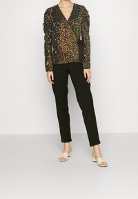 Top nero con paillettes e decorazioni multicolori, design a V, forma attillata, maniche a sbuffo, abbinato a pantaloni neri slim-fit e sandali nude.