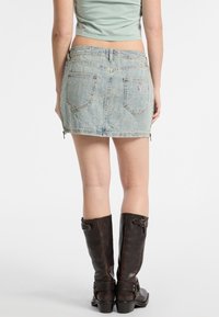 Jasnoniebieska dżinsowa spódnica mini z postrzępionym dołem, tylnymi kieszeniami i bocznymi zamkami, zestawiona z wysokimi brązowymi skórzanymi botkami.