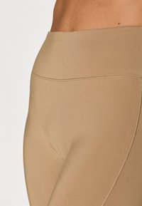 Leggings beiges taille haute avec une texture lisse et de subtils détails de couture, conçues pour le confort et la liberté de mouvement.