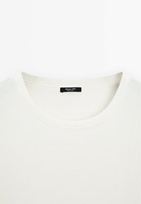 T-shirt bianca in cotone con collo rotondo. Presenta una sottile trama a coste e un'etichetta nera con la scritta "Massimo Dutti" sul colletto.
