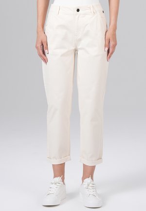 Pantalon cropped couleur crème en coton, avec une texture lisse, des poches avant, deux boutons et des poignets retroussés, associé à des baskets blanches.