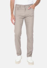 Pantaloni in misto cotone beige con vestibilità slim, caratterizzati da un classico design a cinque tasche e una chiusura con cerniera, abbinati a sneaker bianche.