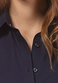 Marineblaues Button-up-Hemd mit Kragen, ausgestattet mit glänzenden schwarzen Knöpfen und dezenten Stichdetails. Glatte Textur, klassisches Design.