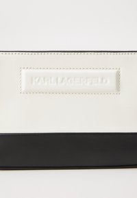 Black and white leather handbag with a smooth texture, featuring a raised logo plaque and contrasting stitching. Rectangular shape.