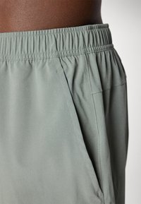 Calções verde-claro com cintura elástica, bolsos laterais e textura de tecido suave. Apresenta detalhes de costura discretos.