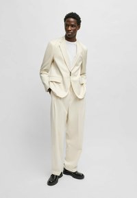 Light beige suit with a tailored jacket and wide-leg trousers. The fabric is smooth; features a single button closure and side pockets. Black shoes.