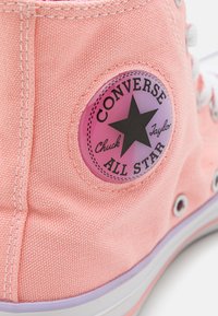Růžové plátěné tenisky Converse All Star s černou nášivkou hvězdy a bílou gumovou podrážkou s růžovými pruhy.