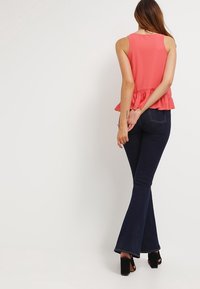 Korallfärgad ärmlös topp med peplumslut, i kombination med mörkblå utsvängda jeans. Outfiten har en mjuk textur och minimalistisk design.