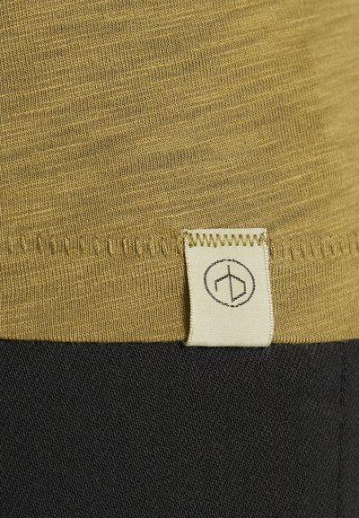 Olive green textile with a textured surface, featuring a white fabric tag stitched at the seam with a circular logo. Black fabric below.
