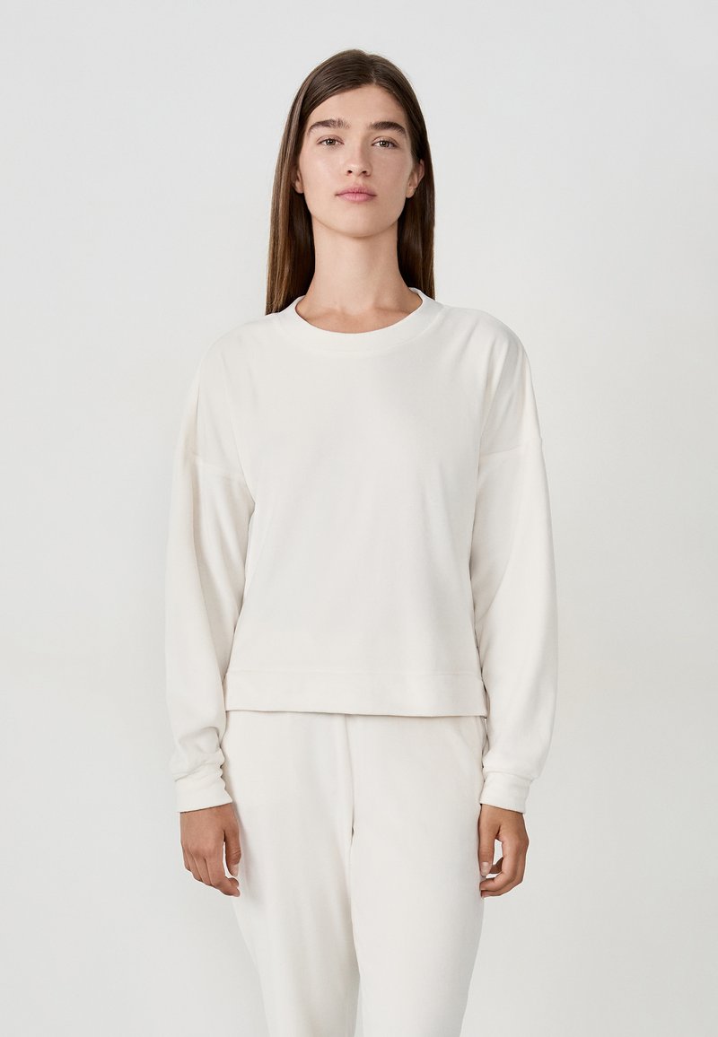 Felpa di colore crema con vestibilità comoda, scollo a girocollo e maniche lunghe. Texture liscia con polsini e orlo a coste. Abbinata a pantaloni coordinati.