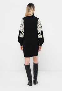 Melnā adīta kleita ar ziedu rakstu baltām piedurknēm, ar augstu apkakli. Stilizēta ar melnu augstas kurpes ādas zābaku līdz ceļgaliem.