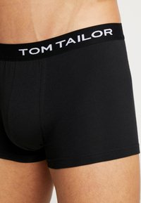 Schwarze Herren-Boxershorts aus weichem Stoff, mit einem breiten schwarzen Bund, der das weiße Logo "TOM TAILOR" trägt. Klassische Passform.