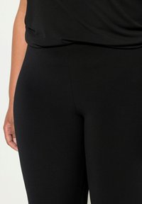 Leggings neri realizzati in materiale elasticizzato con una superficie liscia, dotati di un design a vita alta e una vestibilità aderente.