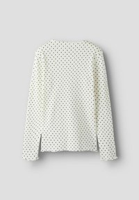 Langærmet, hvid top med små sorte prikker, ribbet struktur, rund halsudskæring og sideslids ved kanten med bølgede kanter.