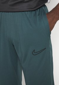 Nike sportbroeken in donkerteal, gemaakt van lichtgewicht stof. Voorzien van een elastische tailleband en een zwart logo op de linker bovenbeen.