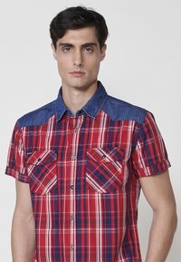 Rot und blau karierter Kurzarmhemd mit zwei Brusttaschen mit Knopfverschlüssen, einem Denim-Kragen und einer lockeren Passform.