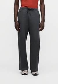 Pantaloni de trening gri închis cu talie cu șnur, design cu picior larg și textură moale, asortați cu pantofi sport în nuanțe neutre.