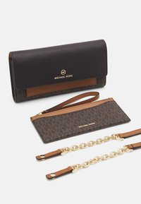 Portafoglio marrone Michael Kors con logo dorato, pochette coordinata e tracolla in catena dorata con estremità in pelle su sfondo bianco.