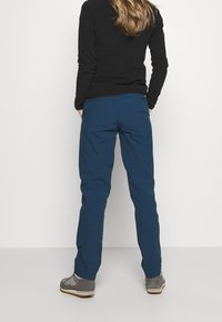 Mörkblå, lätta byxor med avslappnad passform, som har en slät yta och elastisk midja, i kombination med grå, låga skor.